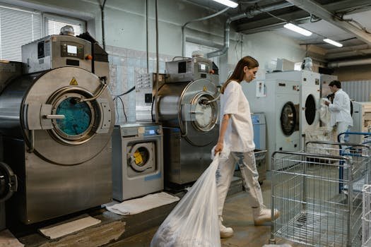 Busy industrial laundry with workers handling large washing machines.